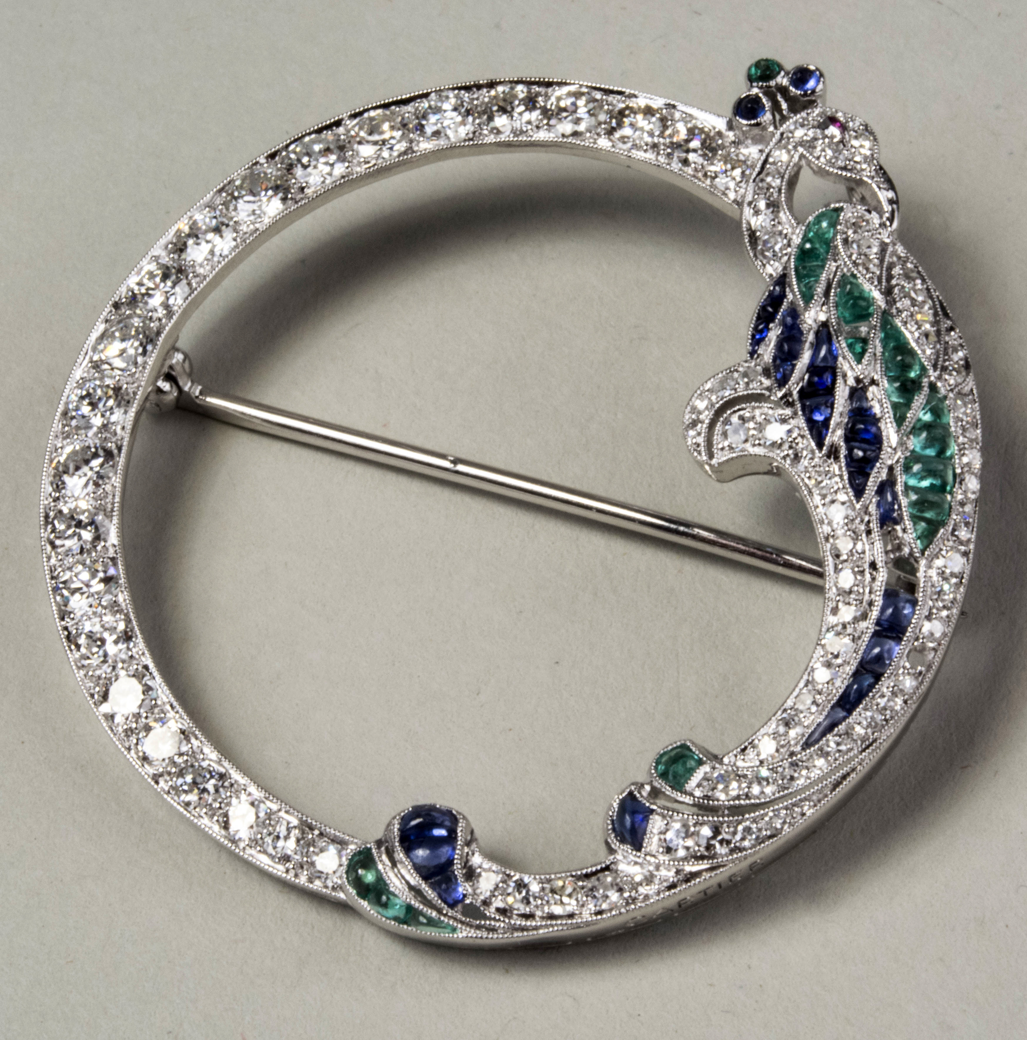 Cartier circle pin, platinum with emerald and sapphire-accented bird of paradise on ring of graduated round diamonds. Est. $8,000-$12,000